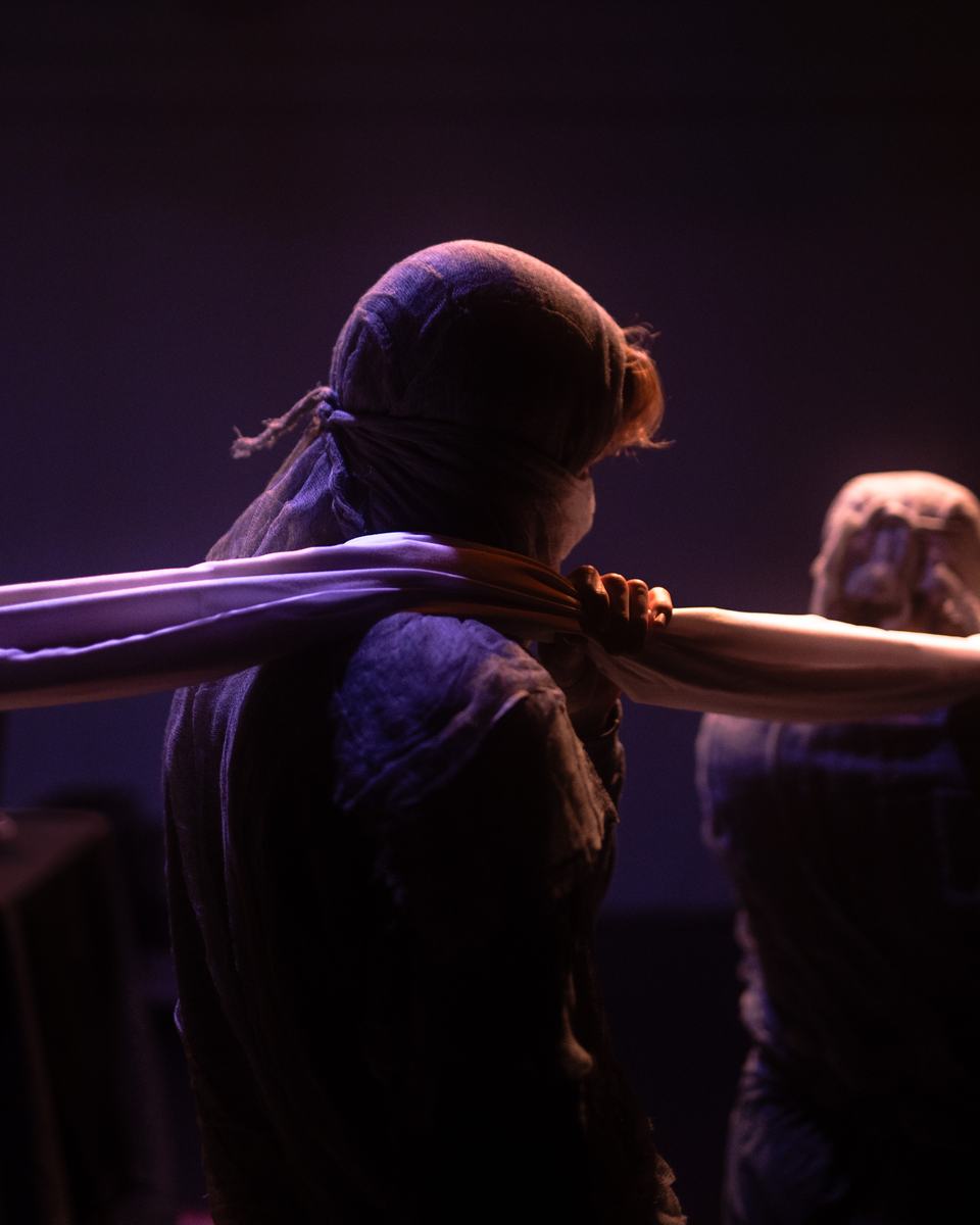 A hooded dancer pulling fabric